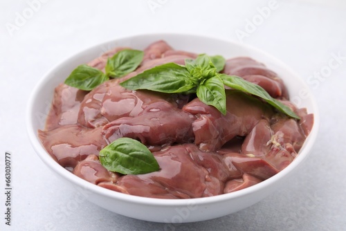 Bowl with raw chicken liver and basil on white table, closeup