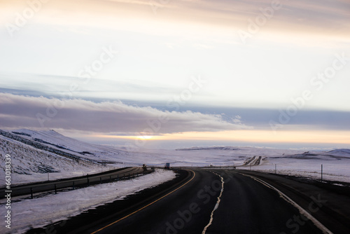 Beautiful winter landscape with a highway between blue snowy mountains, fluffy clouds on a sunset orange sky. Winter snow background. Elk Mountain, Wyoming, USA. Picturesque winter sky © Liudmila