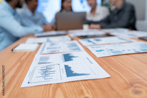 Focus financial dashboard paper showing graphs and chart with blurred background of diverse business people analyzing business data by BI Fintech technology for business marketing indication. Concord