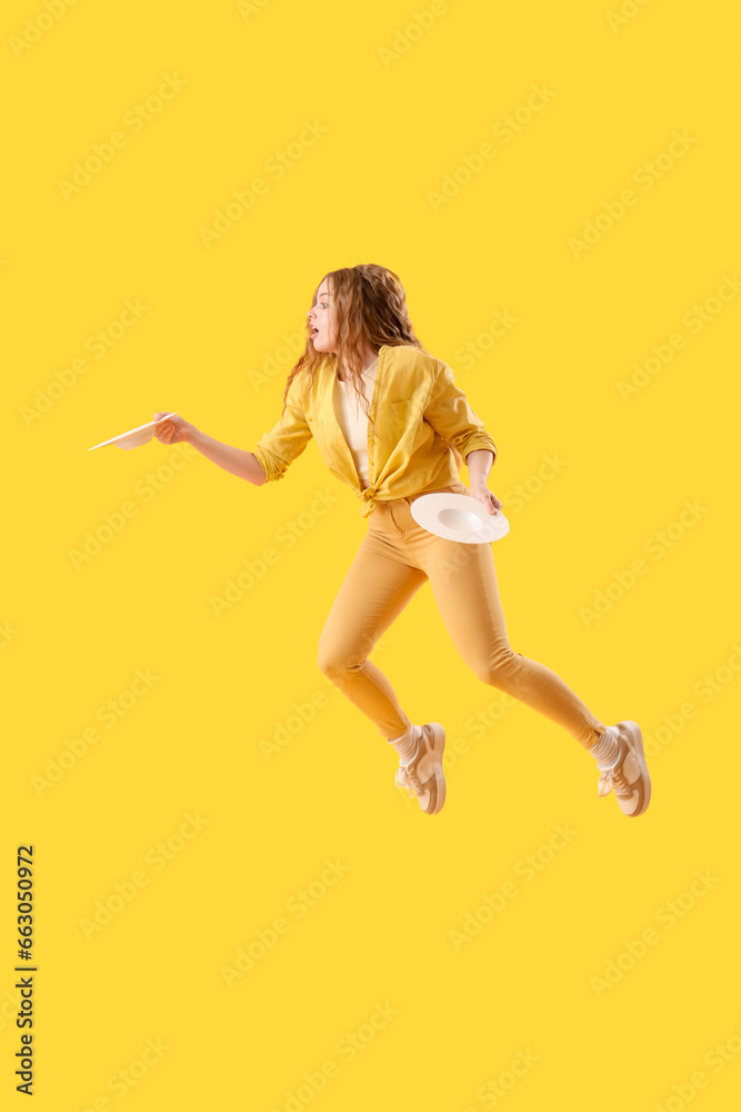 Jumping surprised young woman with empty plates on yellow background Jumping surprised young woman with empty plates on yellow background