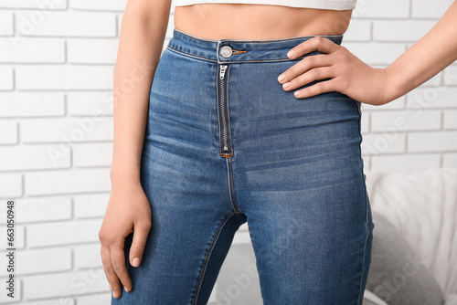 Young woman in stylish jeans near light brick wall