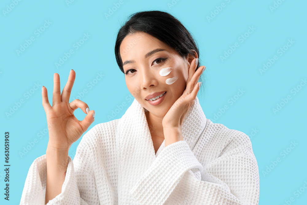 Beautiful Asian woman with cream on her face showing OK against blue background Beautiful Asian woman with cream on her face showing OK against blue background