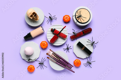 Plaster podiums with lipsticks, different decorative cosmetics and Halloween decor on purple background