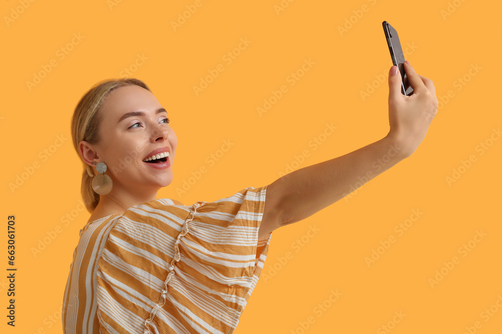 Happy young woman taking selfie with mobile phone on orange background