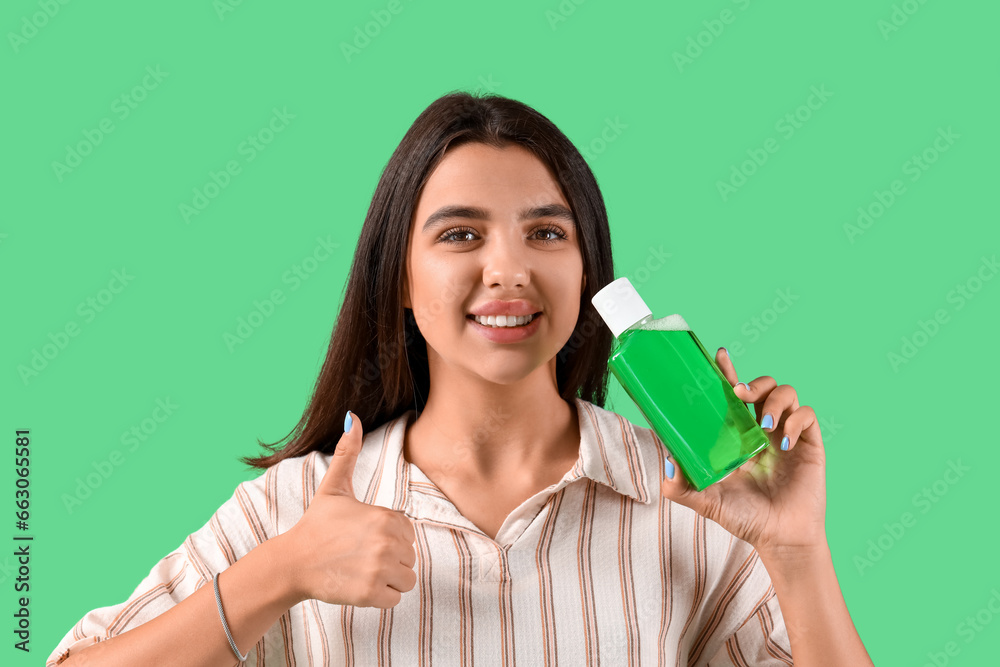Smiling young woman with mouth rinse showing thumb-up on green background Smiling young woman with mouth rinse showing thumb-up on green background