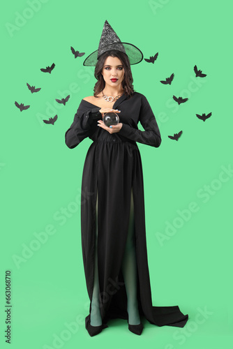 Young witch with crystal ball and bats on green background © Pixel-Shot