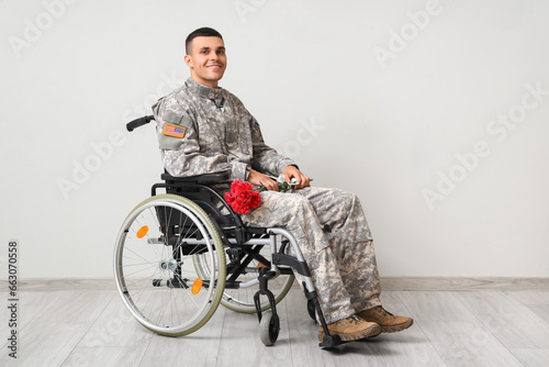 Young soldier in wheelchair with flowers on light background. Veterans Day celebration