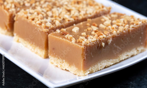 A piece of caramel slice covered with nuts on a white plate