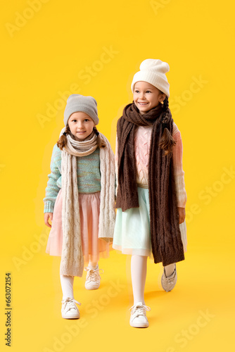 Cute little girls in warm clothes on yellow background