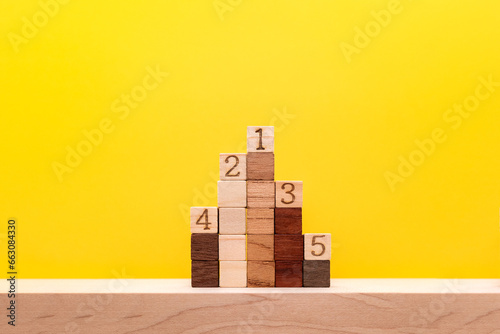 色んな色に分かれているウッドキューブの5位までの表彰台を下から見上げている黄色い背景