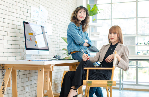 Asian professional successful young female creative graphic designer in casual outfit sitting smiling drawing sketching artwork with pencil when colleague helping thinking ideas in office workstation