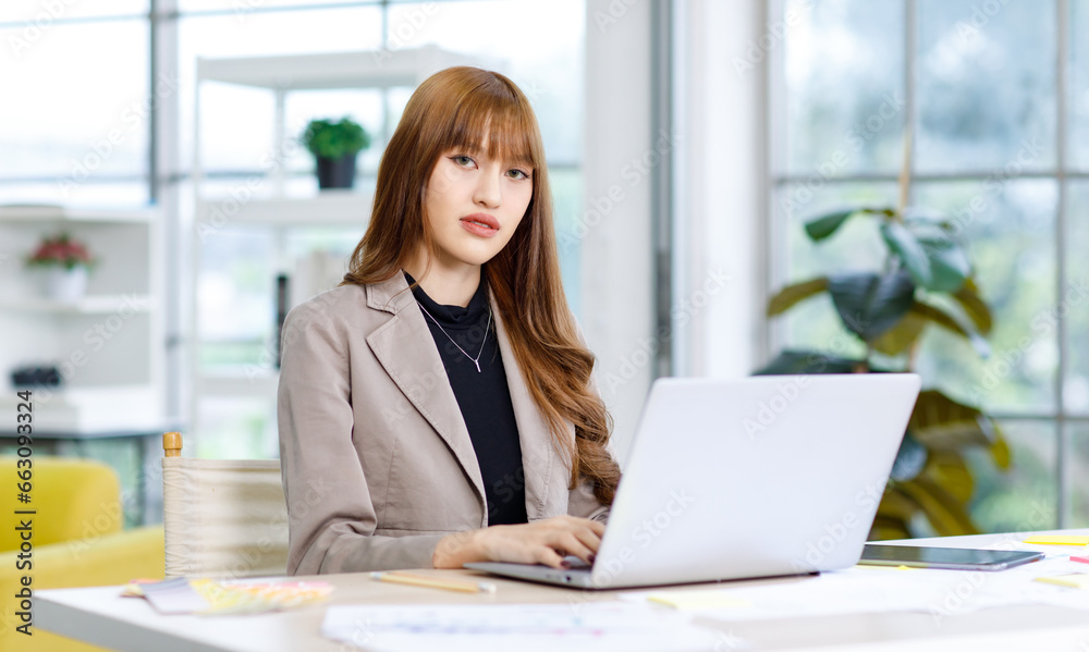 Asian professional successful young female businesswoman creative graphic designer employee in casual fashionable suit blazer outfit sitting working using typing laptop computer at office workstation Asian professional successful young female businesswoman creative graphic designer employee in casual fashionable suit blazer outfit sitting working using typing laptop computer at office workstation