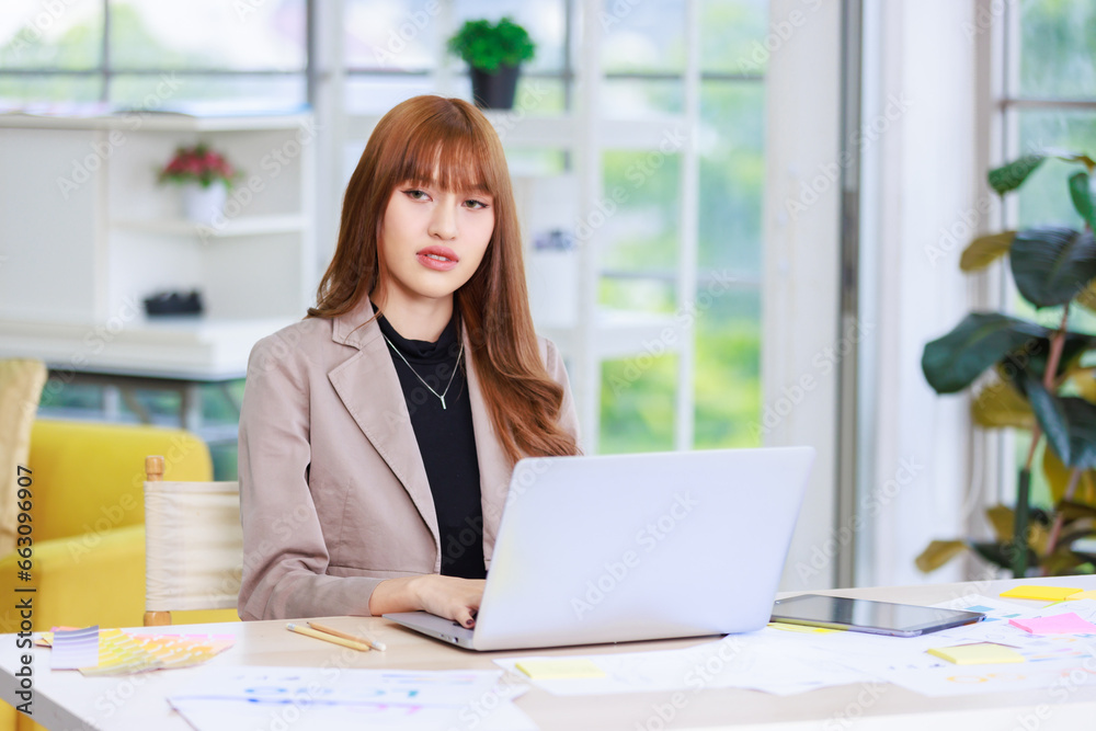 Asian professional successful young female businesswoman creative graphic designer employee in casual fashionable suit blazer outfit sitting working using typing laptop computer at office workstation Asian professional successful young female businesswoman creative graphic designer employee in casual fashionable suit blazer outfit sitting working using typing laptop computer at office workstation
