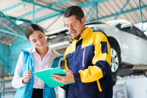 Caucasian white young woman taking her car to garage to have an annual check up and talking or discussing to technician. Automobile repairing and diagnostics service business concept.