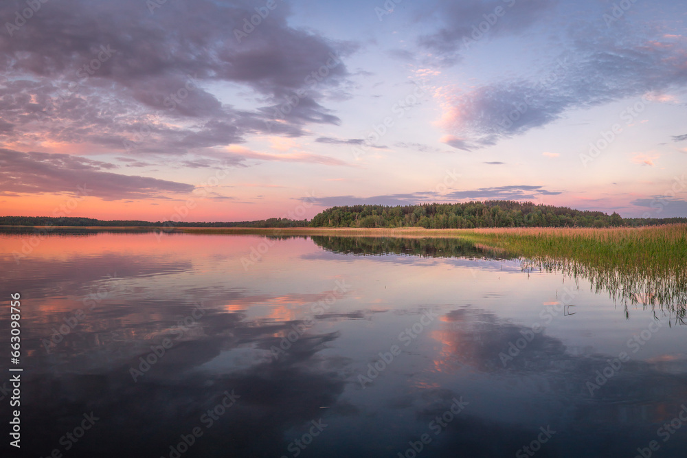 Beautiful panoramic view of sunset on lake Snudy, Braslav kakes, Belarus. The sky is reflected on the surface of the lake red and dark blue colors. A dark forest is visible in the distance.