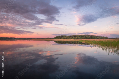 Obraz na płótnie Beautiful panoramic view of sunset on lake Snudy, Braslav kakes, Belarus. The sky is reflected on the surface of the lake red and dark blue colors. A dark forest is visible in the distance. w salonie