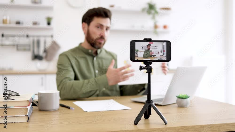 Blur background of caucasian man sitting at desk with laptop and showing financial report on smartphone camera. Competent financier making video lesson about reading and interpreting graphic charts. Blur background of caucasian man sitting at desk with laptop and showing financial report on smartphone camera. Competent financier making video lesson about reading and interpreting graphic charts.