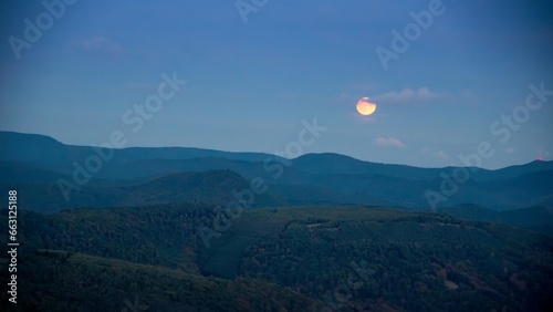 A red beautiful moon over a tranquil mountain landscape with a panoramic view.