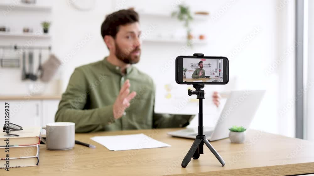 Blur background of caucasian man sitting at desk with laptop and showing financial report on smartphone camera, showing thumb up. Blur background of caucasian man sitting at desk with laptop and showing financial report on smartphone camera, showing thumb up.