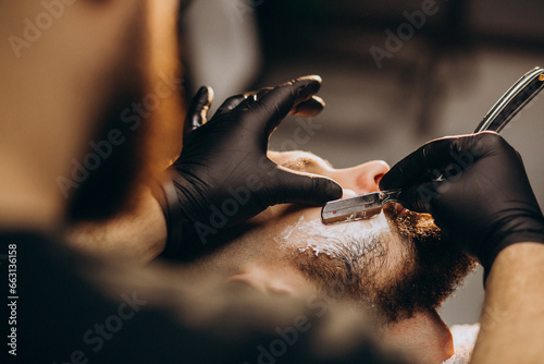 Handsome man cutting beard at a barber shop salon photo