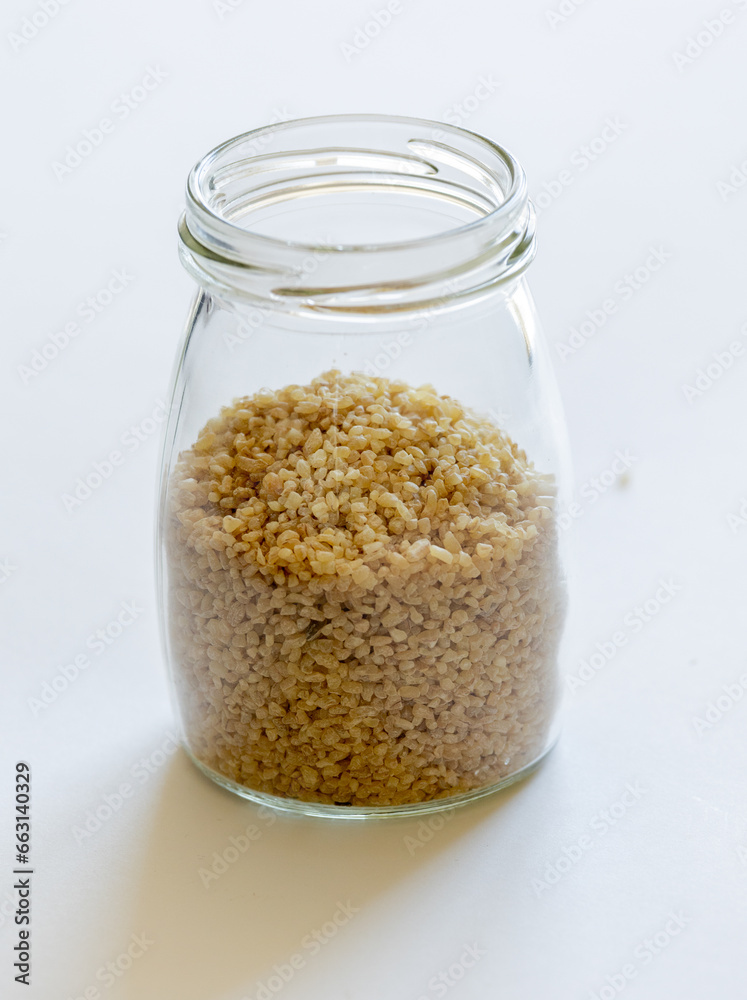 Bulgur grains neatly stored in a glass jar against a clean white background, illustrating food storage Bulgur grains neatly stored in a glass jar against a clean white background, illustrating food storage