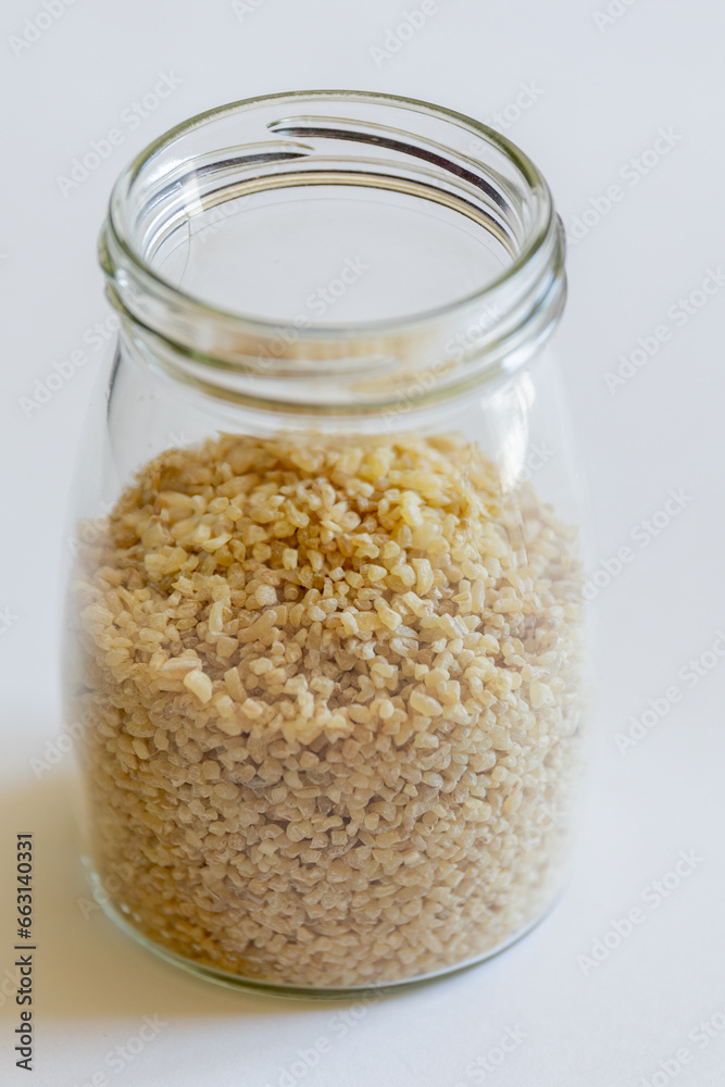 Bulgur grains neatly stored in a glass jar against a clean white background, illustrating food storage