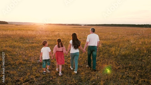 Positive parents with little children walk joining hands across sunset field