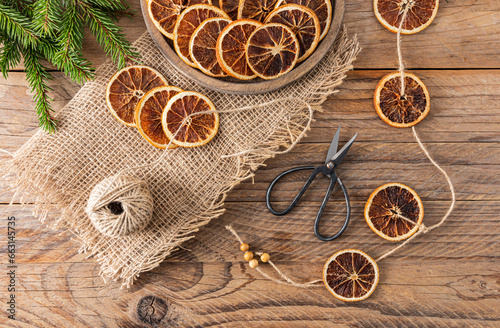 New Year's garland made with your own hands from dried orange slices on a wooden rustic table. Top view. Winter holiday concept. photo