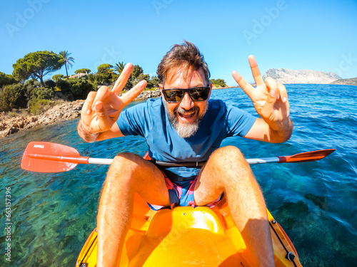 Slika na platnu One cheerful man have fun and pose for a crazy picture sitting inside a yellow kayak canoe  with ocean water and coast in background