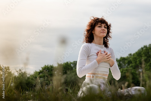 Lady practicing diaphragmatic breathing in the morning. Sports woman doing yoga deeply inhale. Girl hands touch chest training on yogamat outdoors. Professional pranayama master class photo