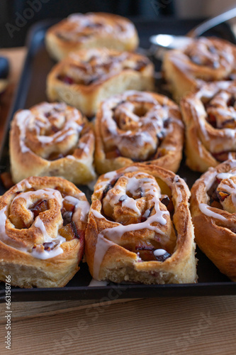 Plum cinnamon rolls fresh baked with sugar glaze on a baking sheet. Selective focus