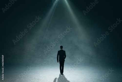 Back view of business man walking in abstract dark interior. Education and smoke room concept.