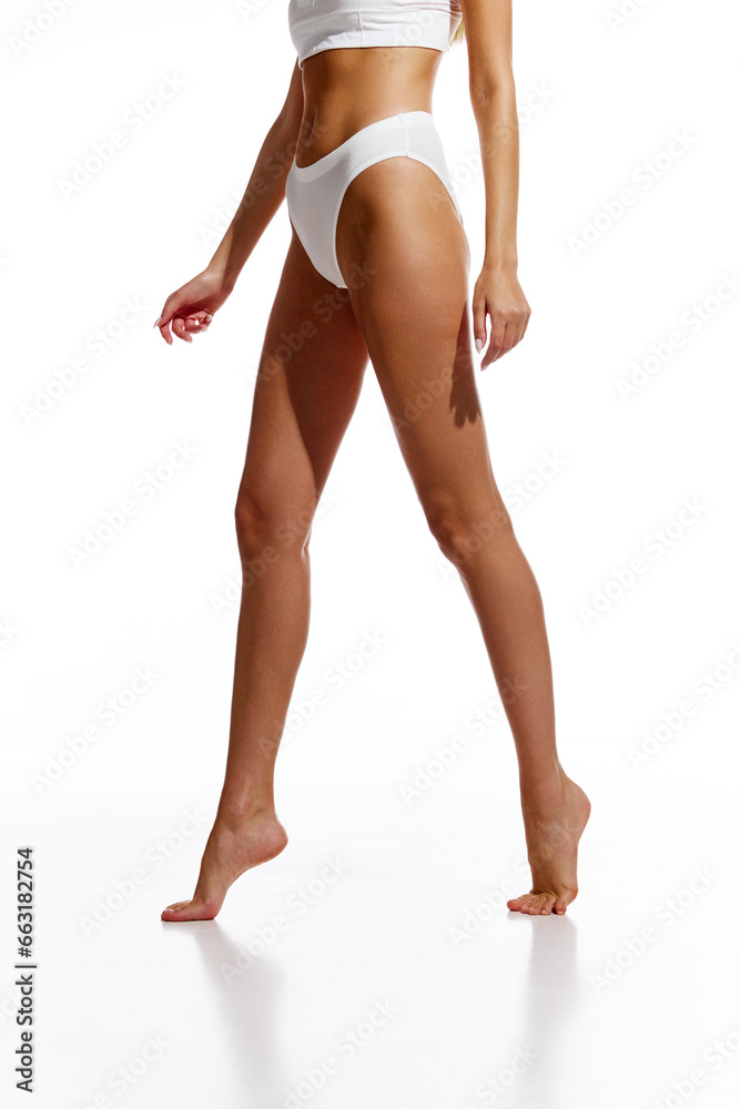 Cropped image of slender, tanned, smooth female legs against white background. Depilation, epilation, laser hair removal. Concept of natural beauty, body and skin care, wellness. Copy space for ad