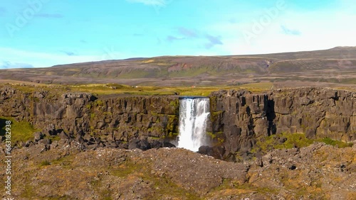 Aerial drone shot above a large Icelandic plain with a large waterfall flowing through a fault on land, sunny weather and blue sky photo