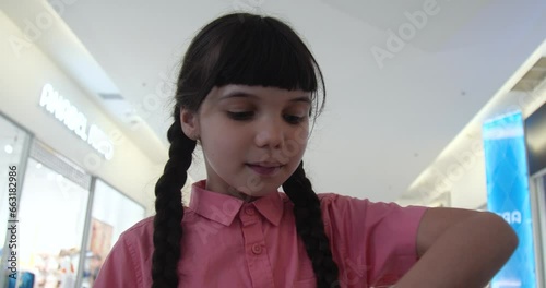 Portrait of little European girl with brown hair braided and wearing a pink shirt eating candy in a store showing thumb up