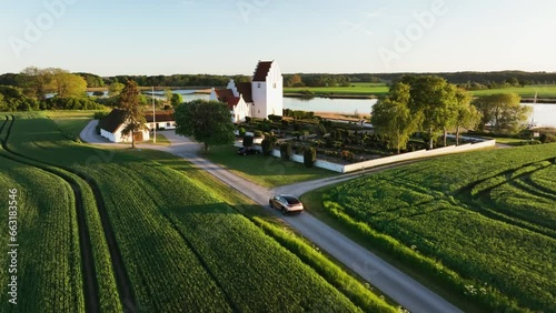 Aerial view following a car arriving at a church, summer sunset on the countryside photo