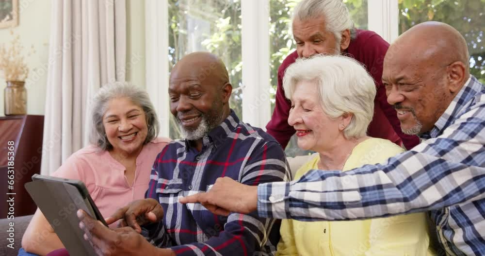 Happy diverse senior male and female friends using tablet together in sunny living room, slow motion Happy diverse senior male and female friends using tablet together in sunny living room, slow motion