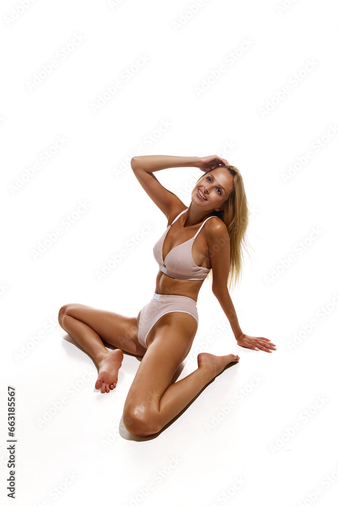 Smiling, beautiful young girl with slim, tanned body sitting in pink cotton underwear against white studio background. Concept of natural beauty, body and skin care, sport, wellness. Copy space for ad Smiling, beautiful young girl with slim, tanned body sitting in pink cotton underwear against white studio background. Concept of natural beauty, body and skin care, sport, wellness. Copy space for ad
