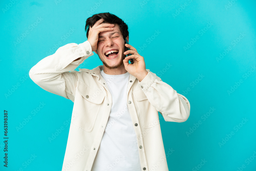 Young Russian man using mobile phone isolated on blue background smiling a lot Young Russian man using mobile phone isolated on blue background smiling a lot