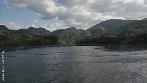 Drone footage over the lakeshore with green dense woods and mountains in the background