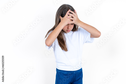 Beautiful little kid girl wearing white T-shirt suffering from strong headache desperate and stressed because of overwork. Depression and pain concept.