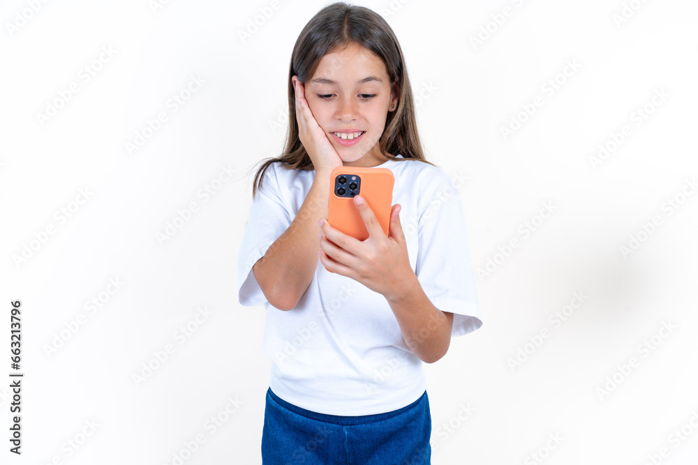 Beautiful kid girl wearing white T-shirt holding in hands cell reading sms using new app 5g Beautiful kid girl wearing white T-shirt holding in hands cell reading sms using new app 5g