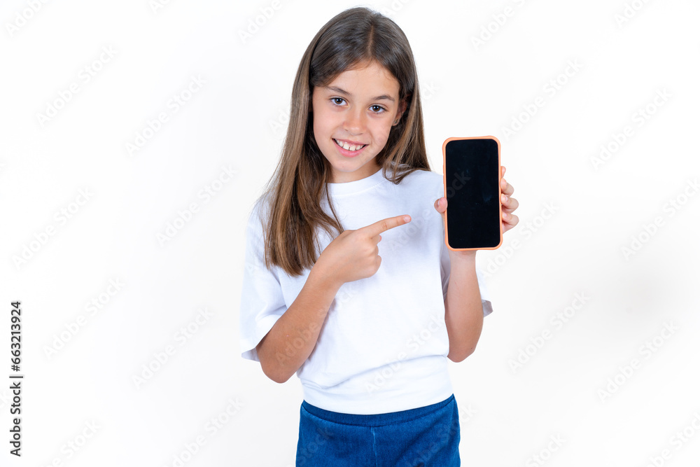 Attractive cheerful Beautiful kid girl wearing white T-shirt holding in hands cell showing black screen Attractive cheerful Beautiful kid girl wearing white T-shirt holding in hands cell showing black screen