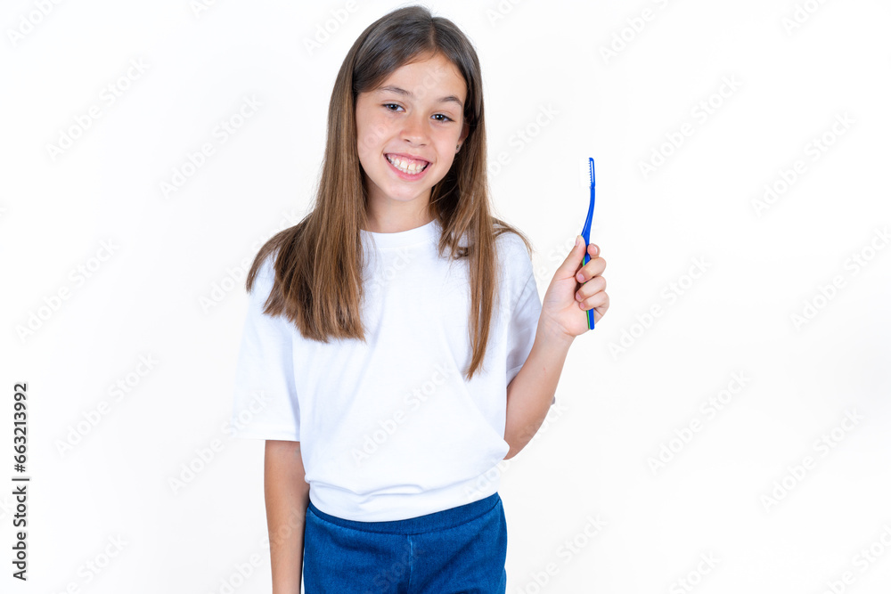 Beautiful kid girl wearing white T-shirt holding a toothbrush and smiling. Dental healthcare concept. Beautiful kid girl wearing white T-shirt holding a toothbrush and smiling. Dental healthcare concept.