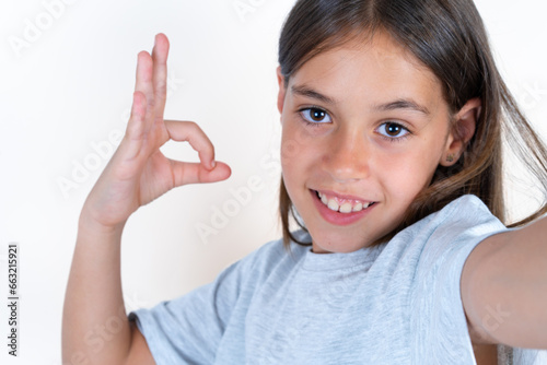 Portrait of pretty cheerful Beautiful little kid girl wearing blue T-shirt make selfie show okey symbol photo