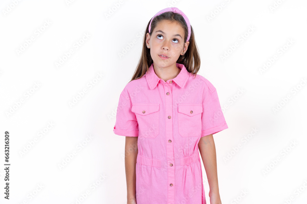 Beautiful little kid girl wearing pink dress looking aside into empty space thoughtful