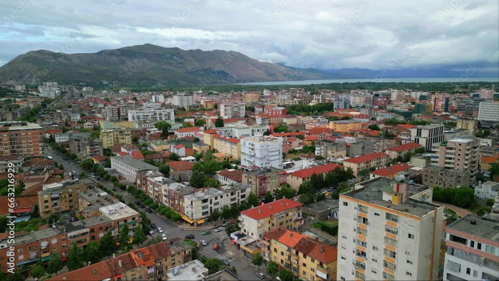Aerial drone forward moving shot over city buildings on both sides of a road in Shkoder or Scutari in northwestern Albania on a cloudy day. Aerial drone forward moving shot over city buildings on both sides of a road in Shkoder or Scutari in northwestern Albania on a cloudy day.