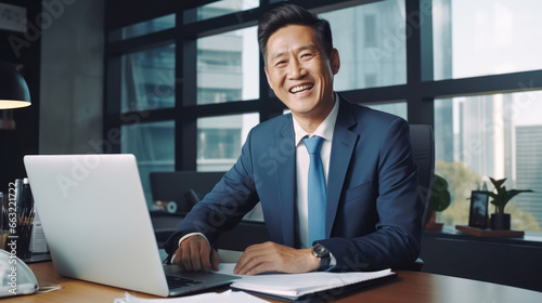 A smiling asian businessman is using a laptop in his office