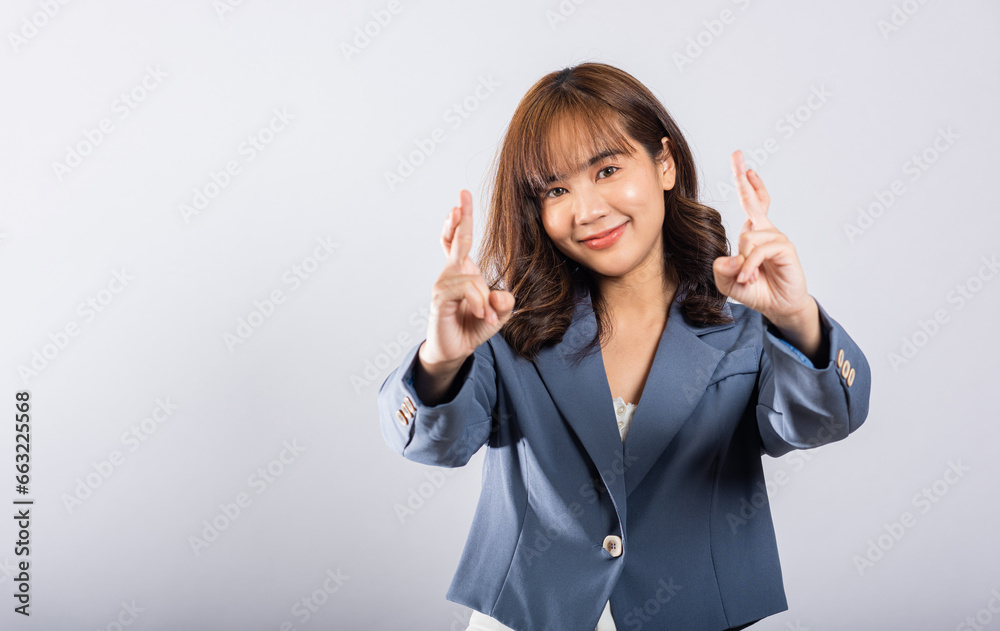 An Asian woman smiles confidently in a studio portrait, her fingers crossed as a sign of hope and good luck. Isolated on white, her expressive face conveys happiness and optimism. An Asian woman smiles confidently in a studio portrait, her fingers crossed as a sign of hope and good luck. Isolated on white, her expressive face conveys happiness and optimism.