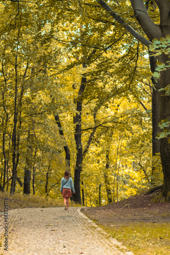 Beautiful brunette woman in brown dress and blue jeans jacket walking in the park. Nature on autumn warm day vacation.